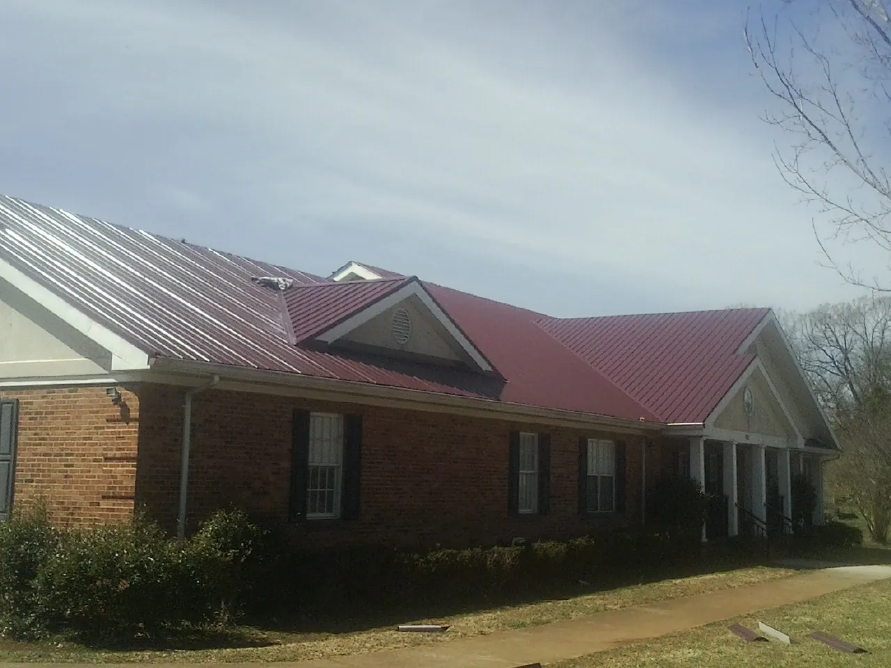 Red metal roof with gabled entries on a long brick building, from a Hail Damage Roof Repair job in Frankenmuth