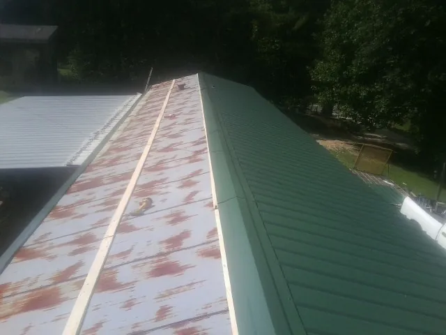 Old rusted panels beside newly installed green metal roofing — Wind Damage Roof Repair by Roofing Brothers in Frankenmuth