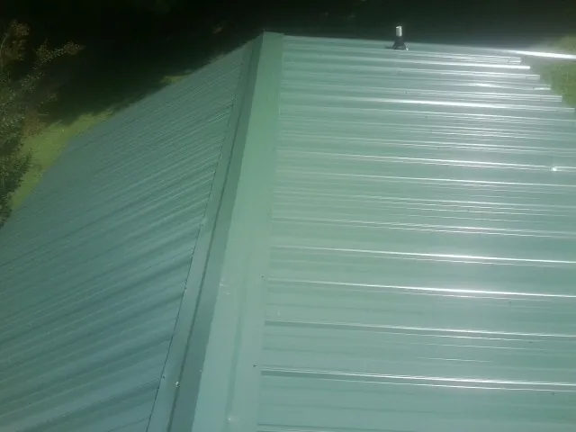New green metal panels meeting at the ridge of a roof — Flat Roof Repair work by our crew in Frankenmuth