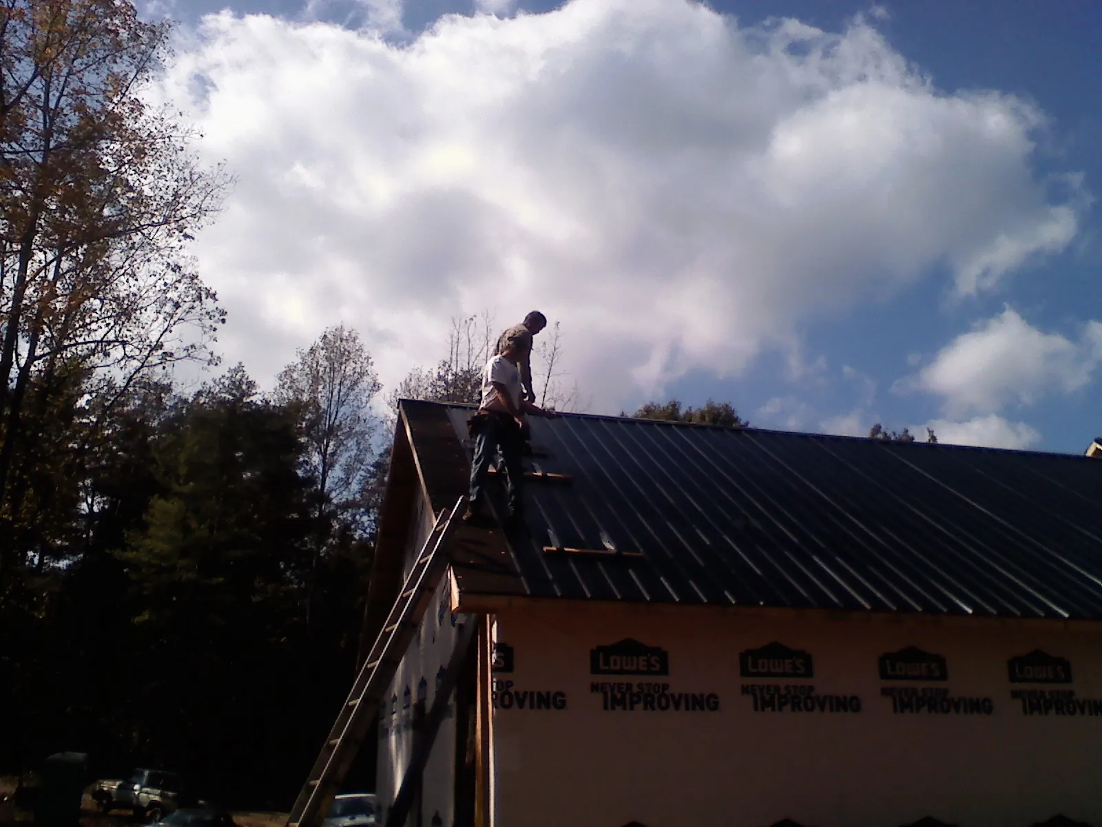 Roofer fastening dark metal panels high against a cloudy sky, from a Roof Inspection job in Frankenmuth