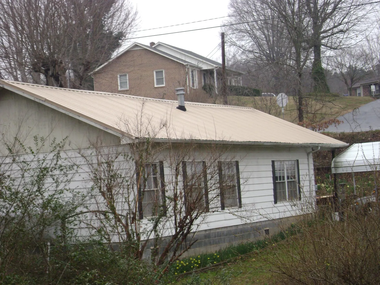 Tan metal roof on a white sided house set into a hillside — Commercial Roofing by Roofing Brothers in Frankenmuth