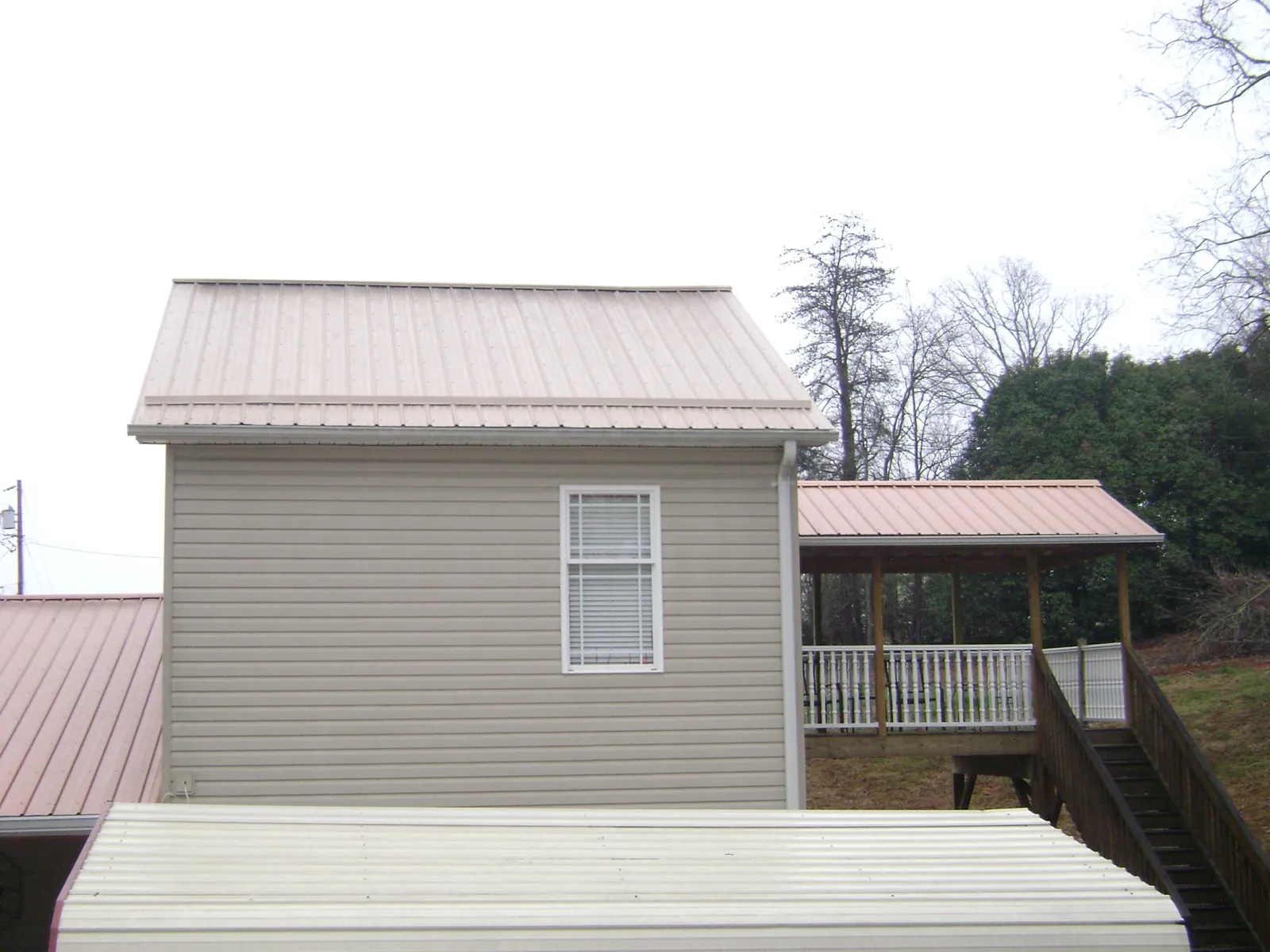 Tan metal roofs on a two story addition and attached porch, from a Roof Replacement job in Frankenmuth